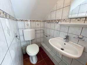 Bathroom features a white toilet, sink, and mirror, set against a backdrop of white and beige tiles.