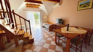 Een gezellige kamer met een houten trap, een bed, een televisie en een eettafel met stoelen.