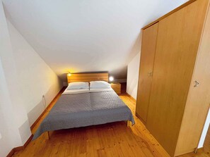 Ein Schlafzimmer mit Bett, Holzschrank und schrägem Dach.