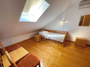 Een klein appartement met één kamer, een schuine kap, een bed, een bureau en een stoel.