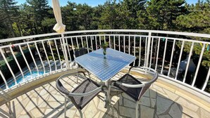 Een balkon met een tafel en stoelen, een zwembad en uitzicht op bomen.