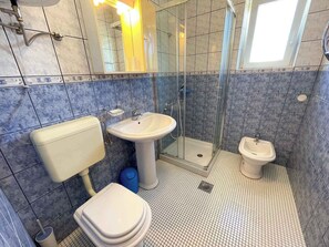 Un baño con inodoro, lavabo y bidé, paredes con azulejos y cabina de ducha.