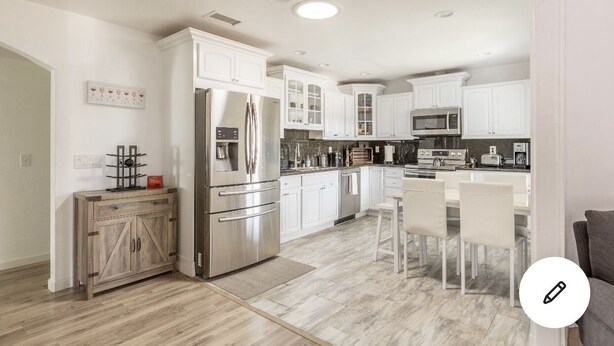 A modern kitchen with white cabinetry, stainless steel appliances, and a central island with chairs. - WindnSealeep (La Jolla)