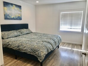 Une chambre à coucher avec un lit, une fenêtre avec des stores et un tableau accroché au mur.
