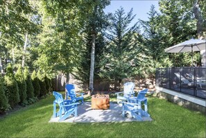 Relax by the fire pit in a serene outdoor space surrounded by Adirondack chairs and lush evergreen trees.