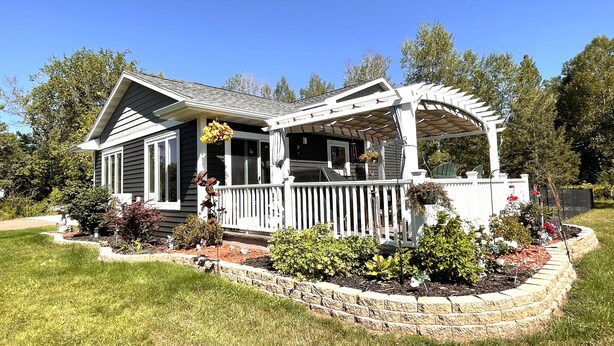 A house with a covered porch, a fenced yard, and a well-maintained garden. - Modern  • Attached garage • Dog friendly • ATV & Sled friendly (Ironwood)