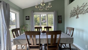 A dining room with a large table, six chairs, a chandelier, and a view through a window. - Modern  • Attached garage • Dog friendly • ATV & Sled friendly (Ironwood)