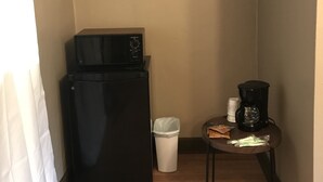 Une petite cuisine équipée avec un réfrigérateur noir, une machine à café posée sur une petite table et une poubelle.