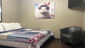Une chambre à coucher avec un lit, une chaise, un téléviseur fixé au mur et un tableau représentant un lapin.