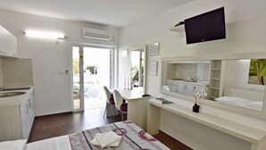 A hotel room with a bed, a desk, a chair, a TV, a mirror, and a bathroom with a sink and toilet. - Studio close to the sea, with pool and jacuzzi (Umag)