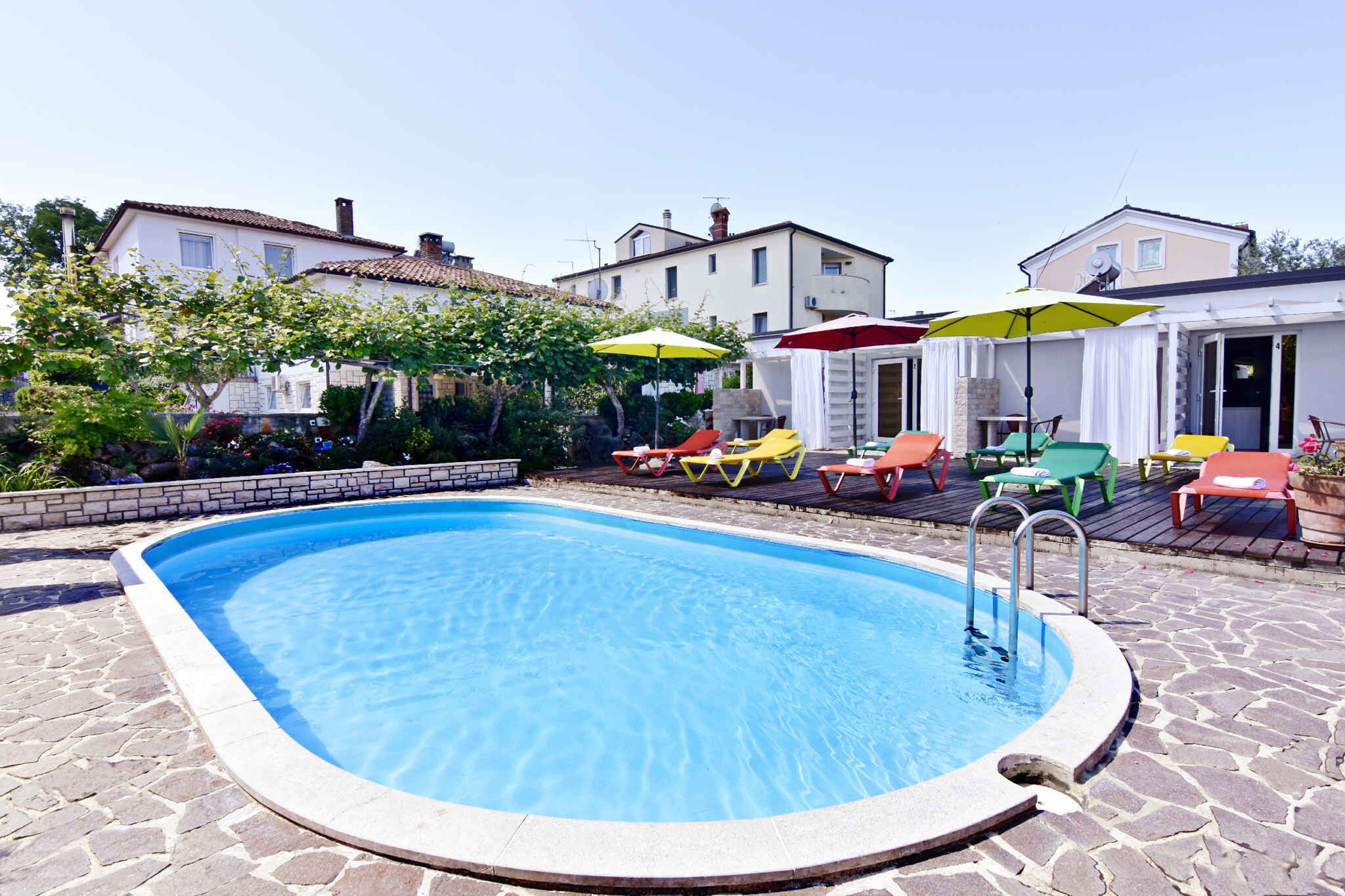 Een zwembad met een stenen terras, omringd door kleurrijke ligbedden en parasols, met huizen op de achtergrond.
