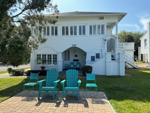 A two-story white house with a number '139' on the front, a covered porch with blue Adirondack chairs, and a small staircase leading to the entrance. - 132A Relaxed Luxury at Casa de Flora in St Augustine  (St. Augustine)