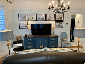 A living room with a TV, blue cabinet, two lamps, a chandelier, and framed pictures on the wall.