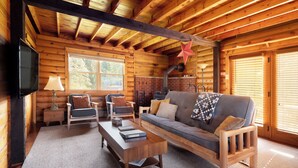 A cozy log cabin interior with a wooden sofa, a television, and a fireplace. - Elk Mountain Vacation Home on 21 Acres (Union Dale)