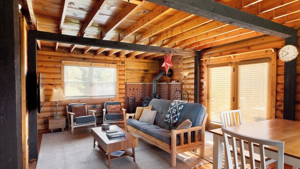 A cozy log cabin interior with a wooden sofa, a dining table, and a fireplace. - Elk Mountain Vacation Home on 21 Acres (Union Dale)