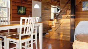 A wooden cabin interior with a dining table, chairs, a staircase, and a bed. - Elk Mountain Vacation Home on 21 Acres (Union Dale)
