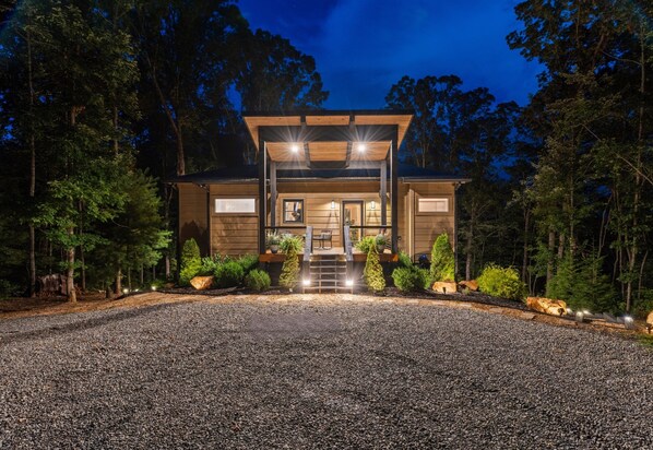 A modern house with a gravel driveway, wooden exterior, and a covered porch with lights.