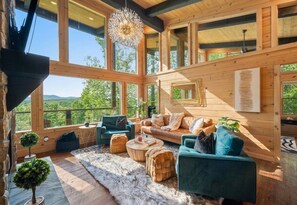 A spacious wooden cabin with large windows, a cozy seating area, and a view of the surrounding forest.