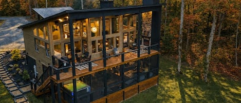 A modern two-story cabin with a deck, surrounded by trees.