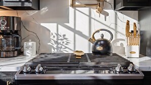 A kitchen with a gas stove, a coffee maker, a kettle, and a cabinet with utensils.