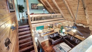 En rummelig loftsuite med højt til loftet, træbjælker, spiseplads, lædersofa og trappe til et opholdsniveau oppe.