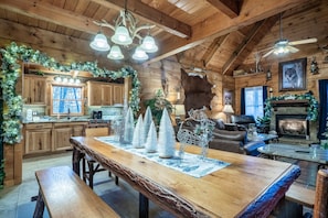 A rustic cabin interior with a wooden dining table, benches, a fireplace, and Christmas decorations. - Upscale, Mtn Views, Hot Tub, & Arcade (Sevierville)