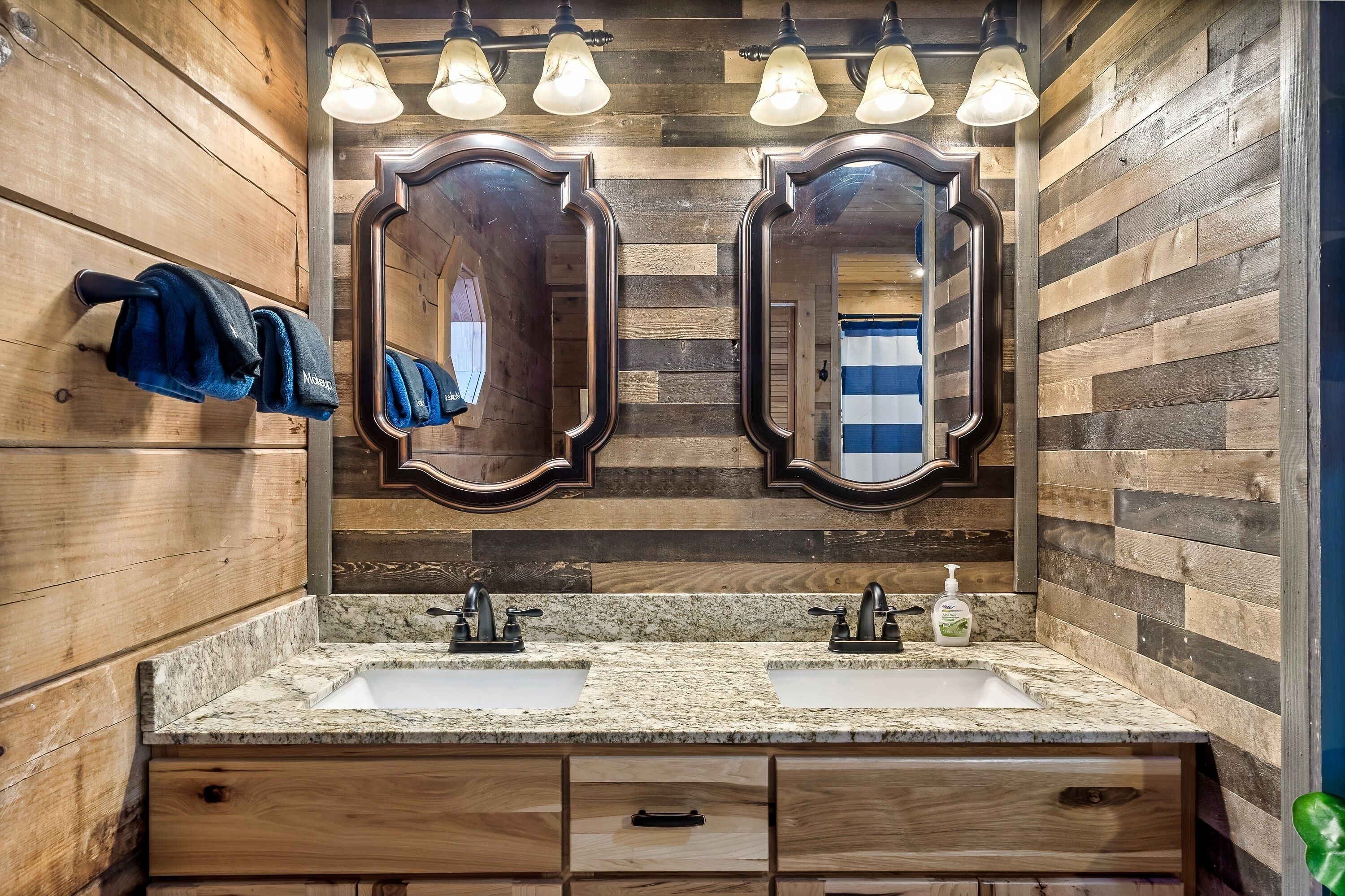 A bathroom with wooden walls, two mirrors, a double sink, and a towel rack.