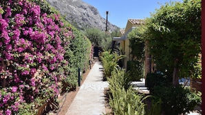 A narrow pathway flanked by lush greenery and vibrant flowers, leading to a building with a tiled roof. - Barbati Beach Villas (Corfu)