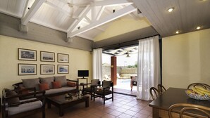 A living room with a sofa, chairs, a coffee table, and a TV. There are framed pictures on the wall and a dining table with chairs. - Barbati Beach Villas (Corfu)