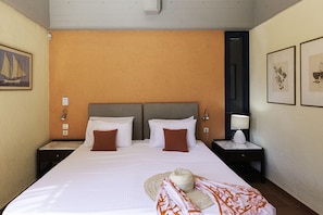Quarto de hotel com uma cama grande, duas mesas de cabeceira, uma luminária fixada na parede e impressões botânicas emolduradas.