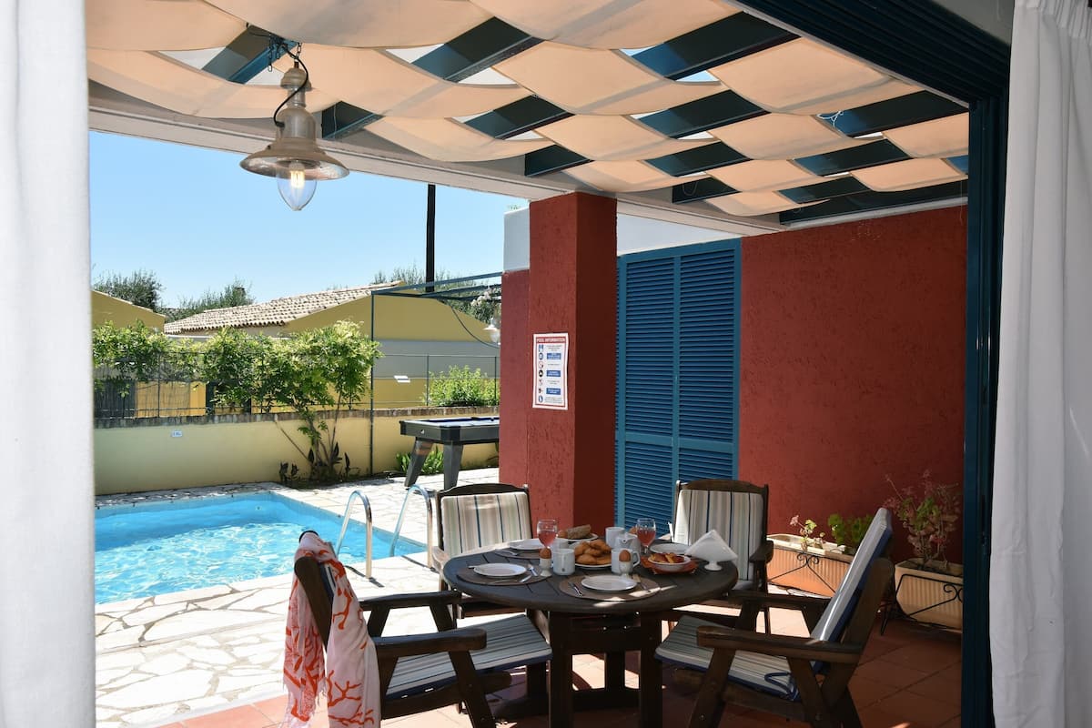 Eine Terrasse mit Pool, Esstisch, Stühlen und einer hängenden Lampe.