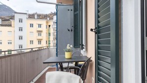 A balcony with a table and chairs, a potted plant, and a door with shutters. - Appartment Lissi a few steps from the centre of Merano (Meran)
