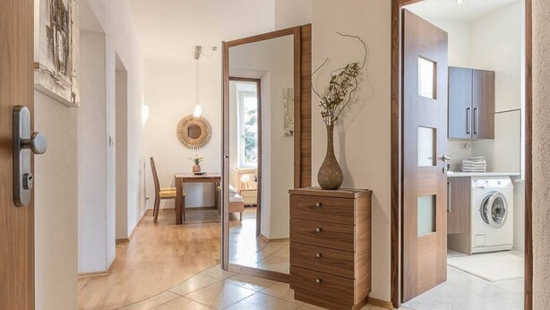 A modern interior with a wooden dresser, a mirror, and a kitchen area with a washing machine. - Appartment Lissi a few steps from the centre of Merano (Meran)