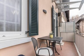 Een balkon met een tafel, stoelen, een plant in pot en een raam met luiken.
