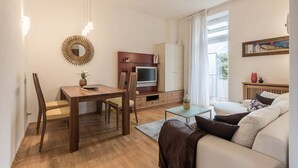 A modern living room with a wooden dining table, a sofa, a TV, and a large window with curtains. - Appartment Lissi a few steps from the centre of Merano (Meran)