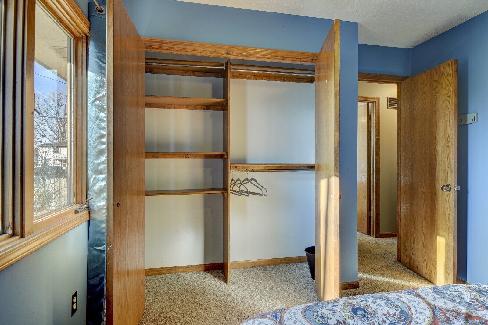A bedroom with a built-in closet, a window, and a door leading to another room.