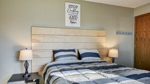 Een slaapkamer met een houten hoofdbord, een bed met gestreept beddengoed, twee nachtkastjes met lampen, en een motiverende quote op de muur.