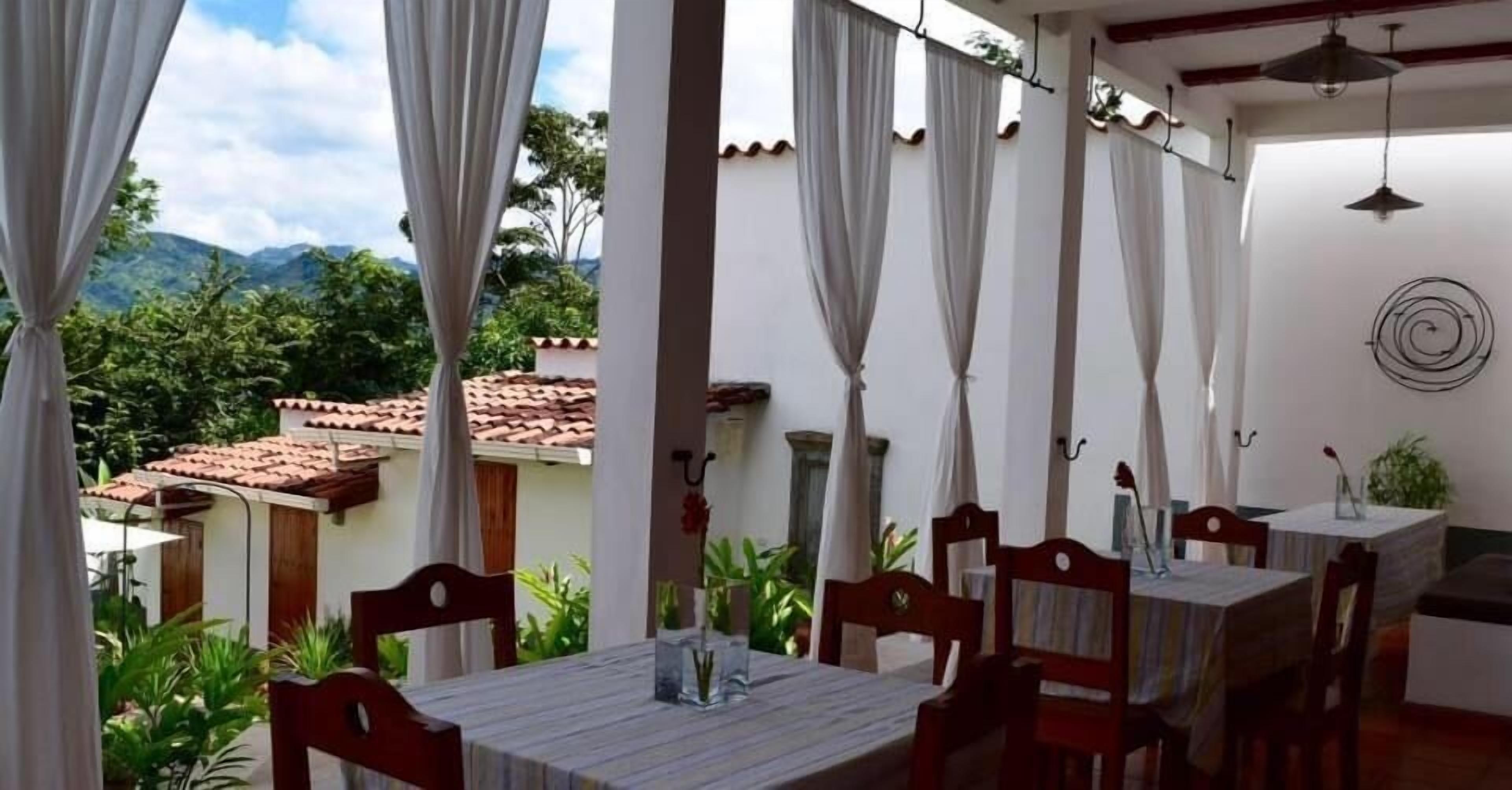 An outdoor dining area with tables and chairs, white curtains, and a view of a mountain landscape.