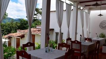 An outdoor dining area with tables and chairs, white curtains, and a view of a mountain landscape.