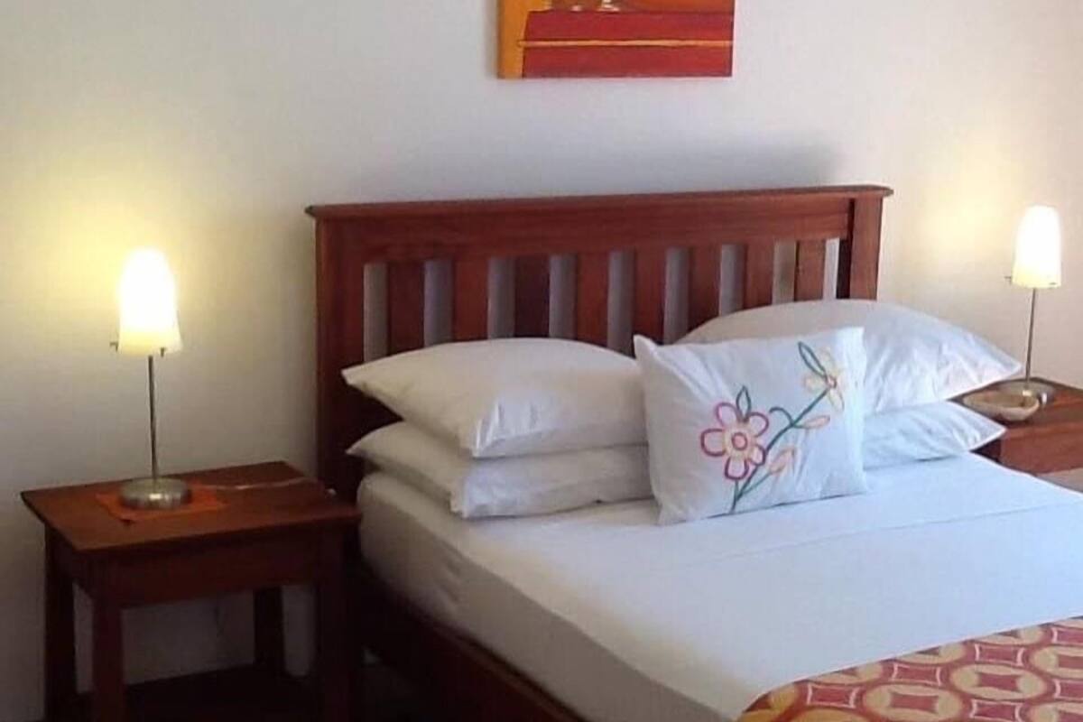 A bedroom with a wooden bed, white bedding, and a floral pillow. There are two bedside tables with lamps.