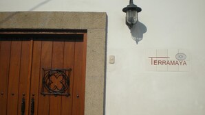 Une porte en bois avec une poignée en métal et une plaque décorative en métal, un luminaire fixé au mur et une enseigne portant le nom « TERRAMAYA ».
