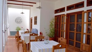 Un espace repas avec des tables et des chaises en bois, des plantes en pot et une vue sur l’extérieur.