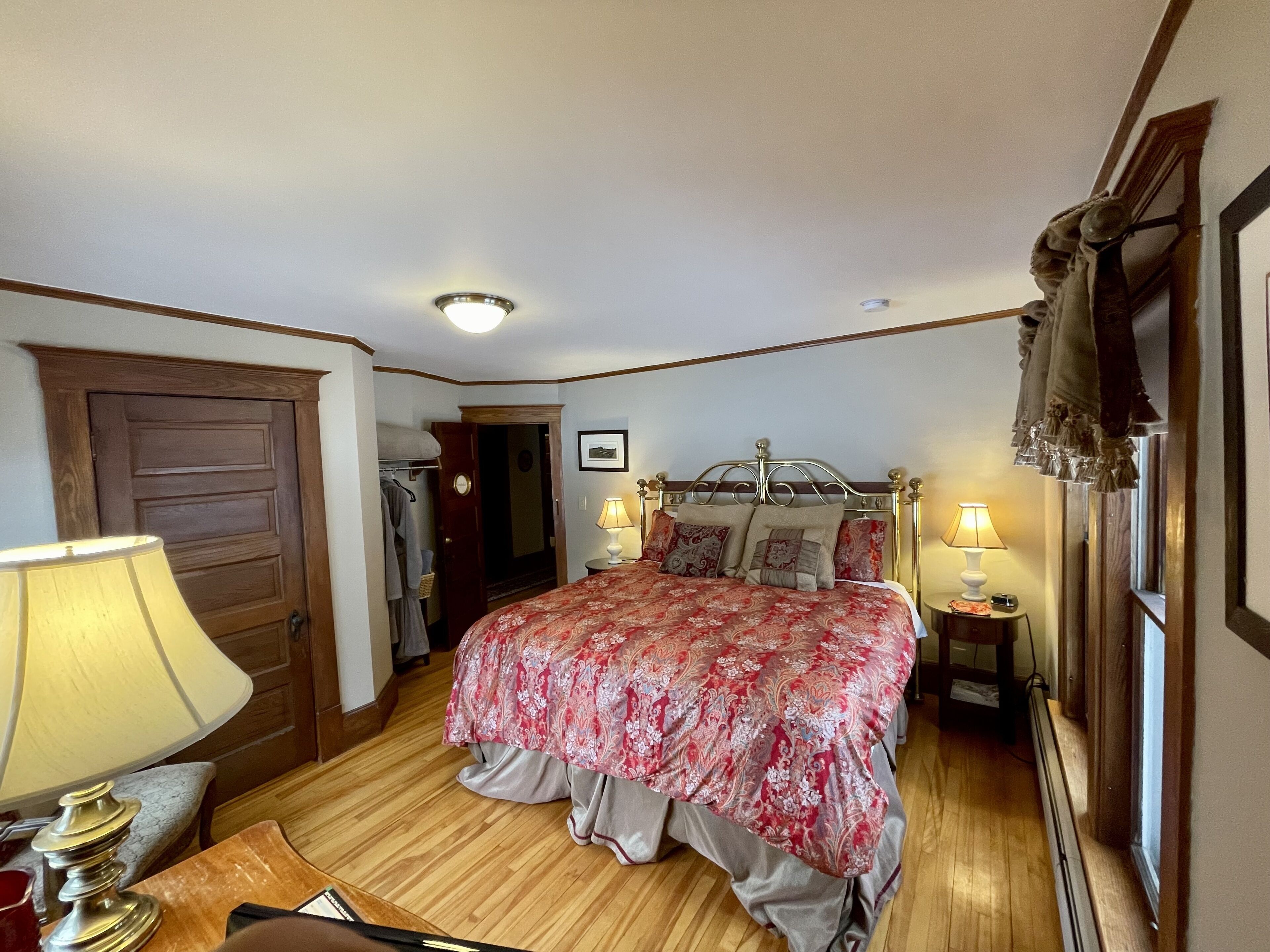 A bedroom with a wooden door, a bed with a floral bedspread, two bedside lamps, and a wooden floor.