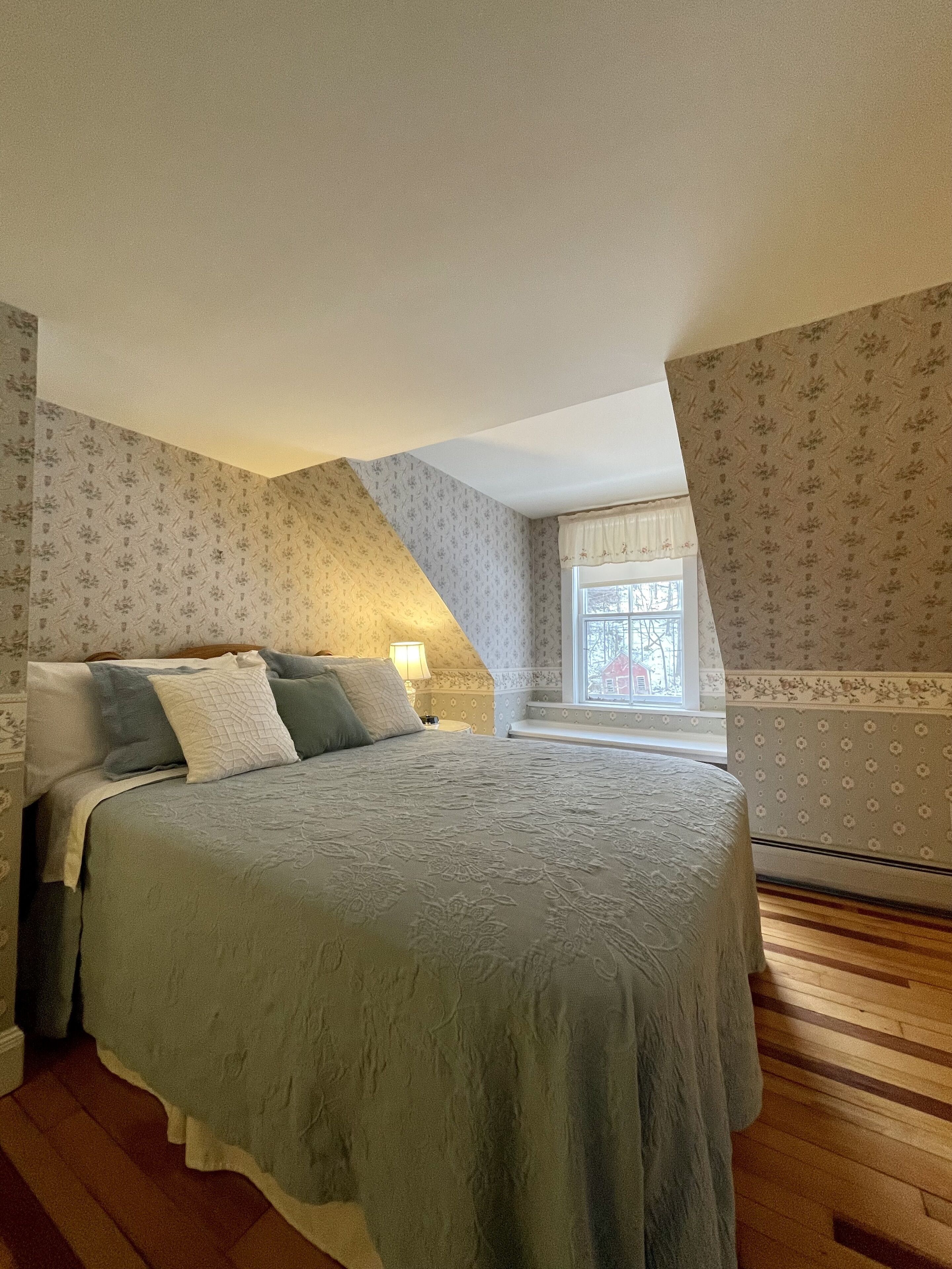 Een slaapkamer met een groot bed, een nachtkastje, een raam met uitzicht en behang met een patroon.