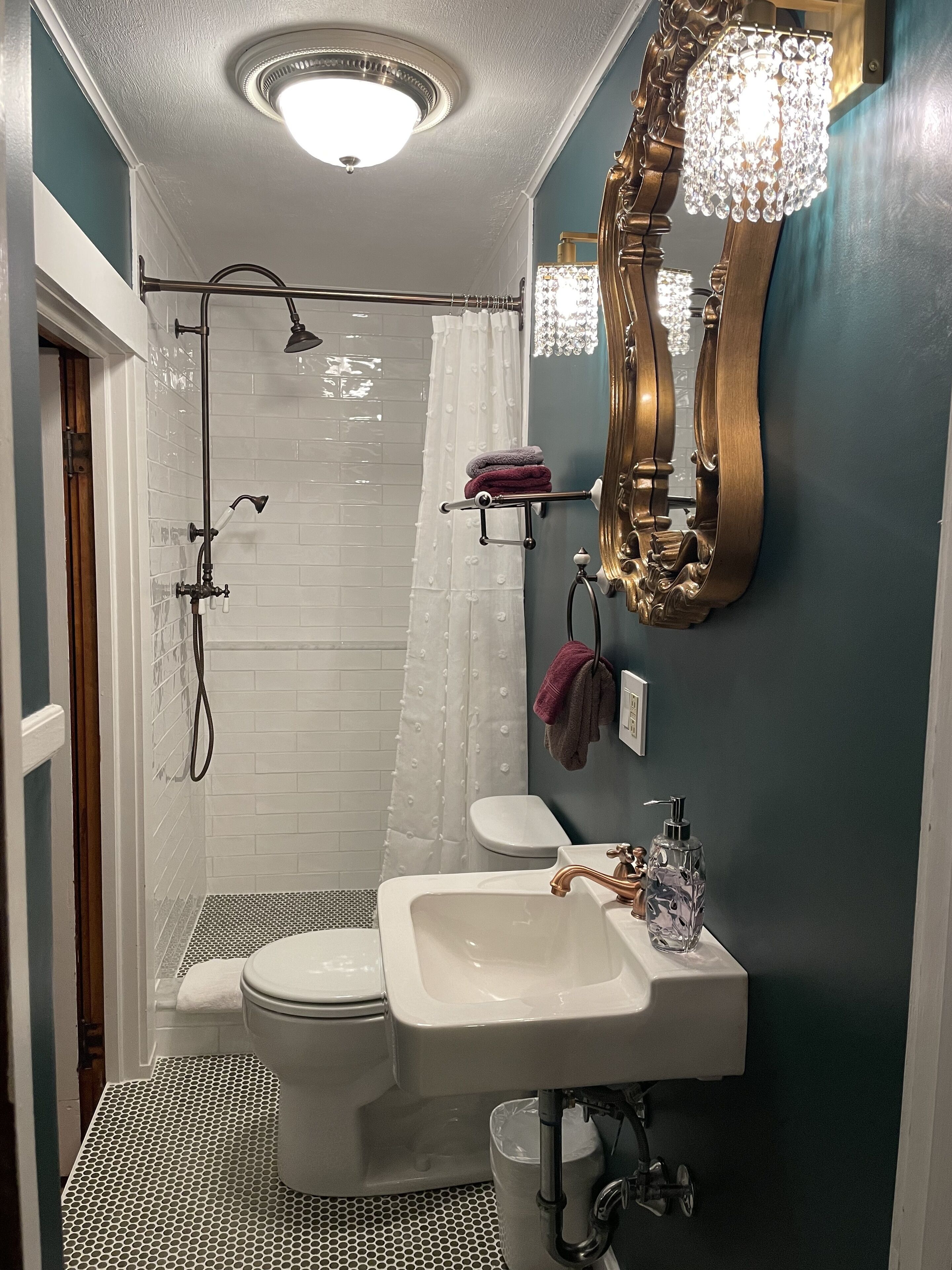 Een badkamer met douche, toilet, wastafel en een spiegel met een kroonluchter.