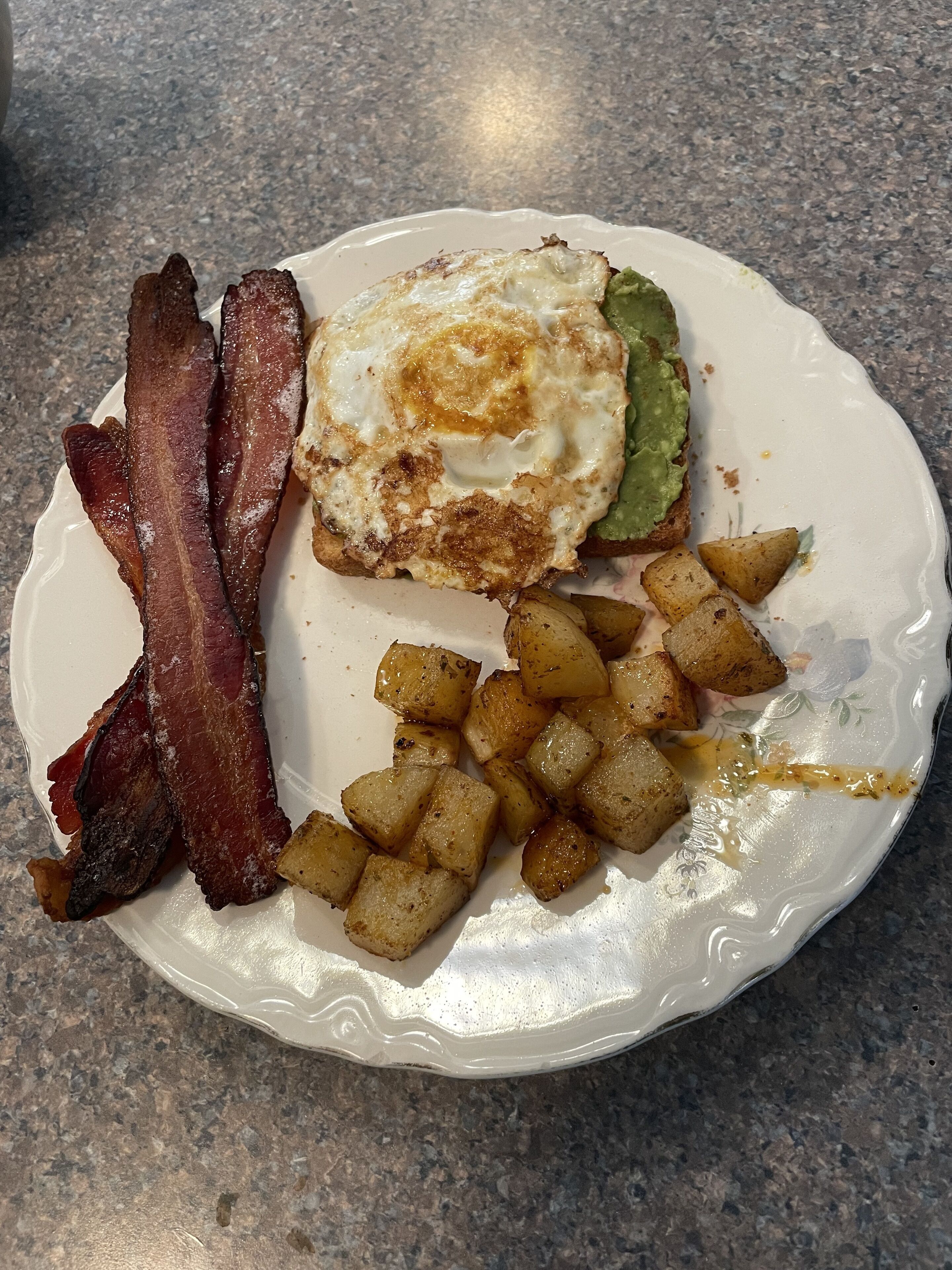 Une assiette composée de lardons, d’un œuf au plat, d’avocat et de pommes de terre rôties.