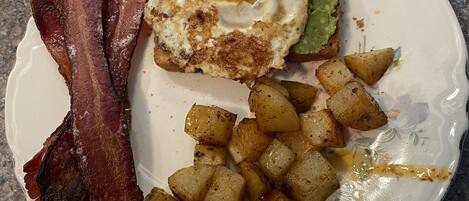 Une assiette composée de lardons, d’un œuf au plat, d’avocat et de pommes de terre rôties.