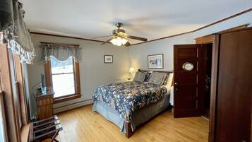 A bedroom with a bed, a ceiling fan, a window with curtains, a desk with a lamp, and a door with a nameplate.