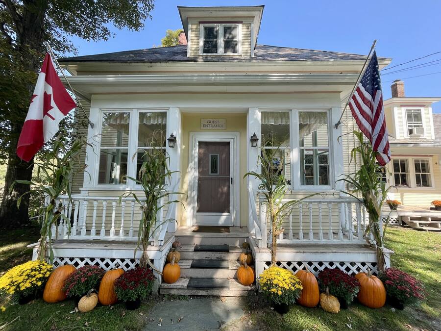 A two-story house with a porch, a guest entrance sign, and two flags.