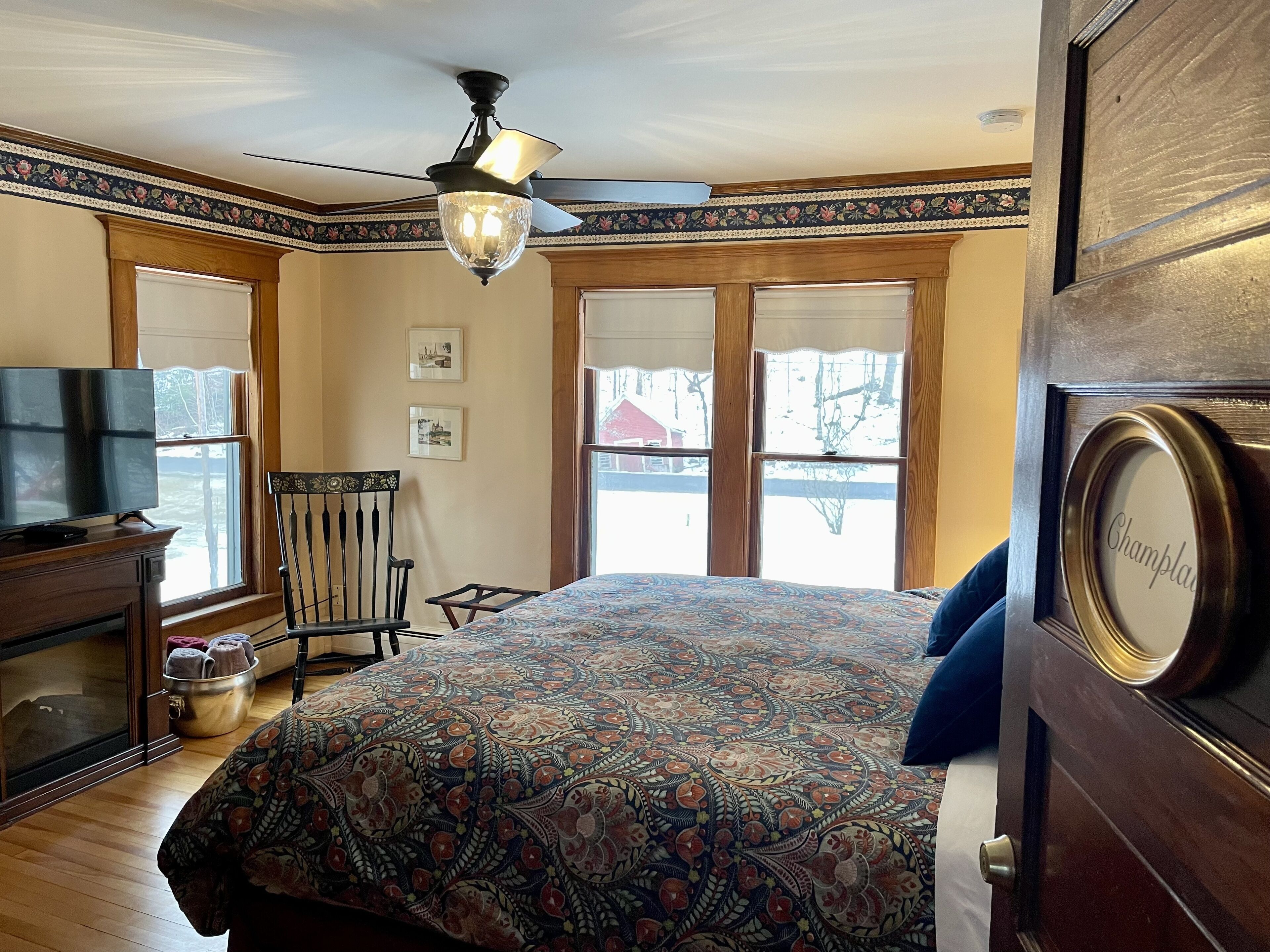 Un dormitorio con colcha estampada, cómoda de madera, televisor y una silla.